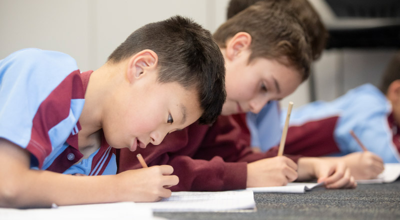 Students writing in a workbook on the floor of the classroom at St Bernadette's Primary School Dundas Valley