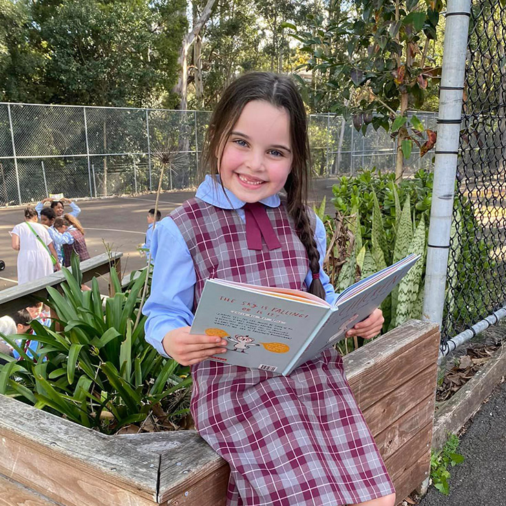 Student in her winter uniform reading in the playground at St Bernadette's Primary School Dundas Valley